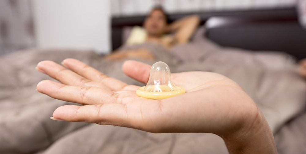 A woman holding a condom who is about to give her partner an erotic massage