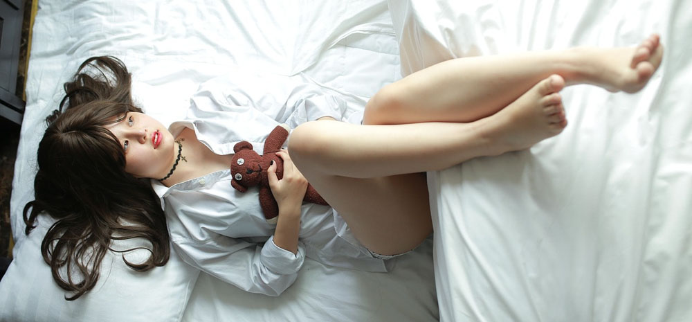 A Chinese massage therapist lay down on a bed holding a teddy bear