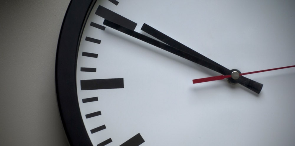 A white analogue clock hanging from a wall